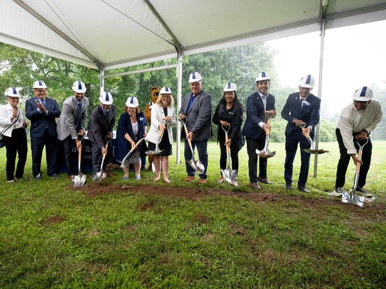 People shoveling dirt under a tent to break ground for new construction